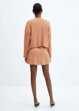 Falda corta de punto canalé color salmón, con cintura elástica y diseño evasé, sin cierre.