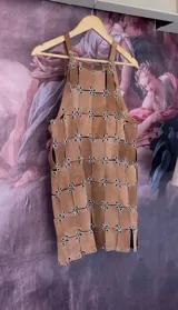 Vestido corto sin mangas, color marrón, confeccionado artesanalmente con múltiples tiras de cuero genuino unidas por ojales metálicos plateados, creando un efecto de malla o armadura.