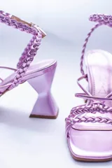 Sandalias negras con tiras lisas y trenzadas en el empeine, y una tira trenzada que se ajusta al tobillo con hebilla. Tienen un tacón geométrico.