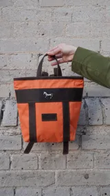 Mochila pequeña color borgoña con detalles en cuero marrón, asa de mano y correas ajustables.