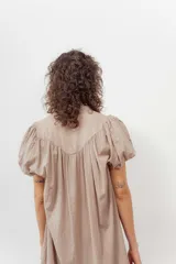 Vestido color beige con botones frontales, cuello camisero, mangas cortas abullonadas y falda con volantes.