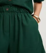 Short blanco de corte runner evasé, con cintura elástica fruncida y un botón decorativo. Presenta bolsillos laterales y un calce suelto.