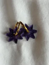 Aros de acrílico en forma de estrella color morado con detalles brillantes y aro dorado.