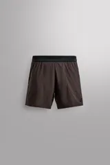 Shorts deportivos marrones de tejido técnico ligero y elástico con diferentes estructuras. Tiene forro interior, cintura elástica ajustable con cordón, bolsillos frontales, bolsillo trasero con cierre, aberturas laterales y logo estampado en la pierna.