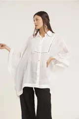 Camisa blanca de lino con corte amplio, cuello camisero y mangas 3/4 con detalle de puntilla en el borde.