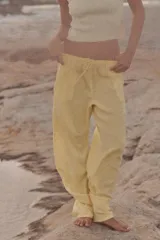 Pantalón de mujer color amarillo pálido, de corte ancho y tejido fluido. Tiene tiro medio, cintura elástica ajustable con cordones, bolsillos laterales y falsos bolsillos de vivo en la espalda.