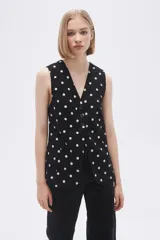 Chaleco largo sin mangas negro con estampado de lunares blancos, cuello en V y corte entallado.