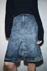 Falda midi de denim, tiro medio, color azul claro con efecto lavado (acid wash). Diseño recto con abertura frontal y cierre de cremallera y botón.