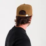 Gorro gris con visera y laterales negros, con logo de Caterpillar bordado en amarillo y negro sobre un cuadrado con rayas horizontales amarillas. Ajuste trasero con hebilla metálica.