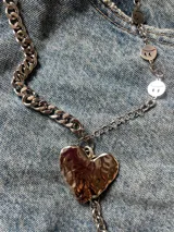 Collar metálico plateado con dije de corazón y de flor. La cadena está formada por dos modelos distintos: una con caritas sonrientes y otra de eslabones gruesos.