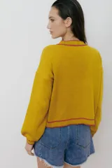 Cárdigan tejido en 50% algodón y 50% acrílico, color crema, con pespuntes tejidos en contraste color borgoña y bordado de limón en el pecho. Tiene cuello con volados, cierre frontal con botones y corte relajado.