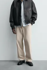 Pantalón chino color beige, de corte relaxed fit, confeccionado en tejido de mezcla de algodón y lino. Cuenta con bolsillos delanteros y traseros de vivo. Cierre frontal con cremallera y botón.