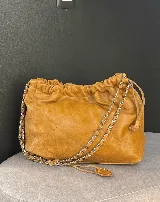 Bolso tipo hobo de cuero color caramelo con diseño acolchado y cierre fruncido. Tiene correa de cadena plateada y herrajes plateados.