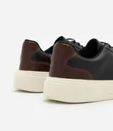 Championes casuales de cuero negro con cordones elásticos y recortes en marrón en el talón. Suela blanca.