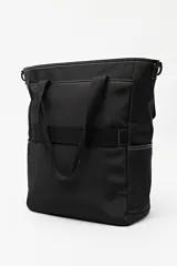 Cartera tote negra con doble asa superior y correa desmontable y regulable. Cuenta con un bolsillo frontal con solapa y cierre, y bolsillos laterales. Presenta pespuntes blancos decorativos y un logo cuadrado en la parte inferior.