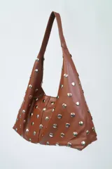 Cartera tipo hobo de cuero color marrón con apliques de tachas plateadas.