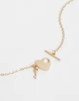 Cadena corta dorada con dije de corazón y llave de metal.