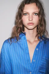 Camisa celeste con rayas verticales blancas, de corte oversize, cuello solapa, manga larga con puños y bolsillo de plastrón en el pecho.