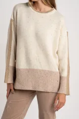 Sweater de lana color crema con efecto tweed, de calce oversize y cuello redondo. Presenta bloques de color en la parte inferior, puños y laterales de las mangas en tono beige con textura acanalada y detalles brillantes.