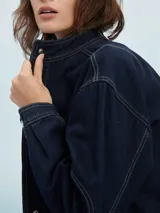 Campera corta de jean azul oscuro con costuras en hilo color crema, cuello mao y cierre con botones metálicos.