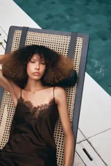 Vestido corto de satén color blanco, con tirantes finos, escote en pico y bajo asimétrico con abertura. Detalle de encaje negro en escote y ruedo.