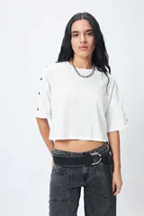 Remera blanca cropped de mangas cortas amplias con ojales metálicos a lo largo de las mangas.