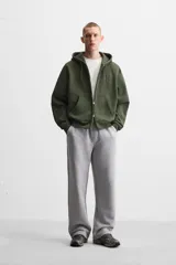 Sudadera negra relaxed fit de algodón compacto con interior en rizo, cuello con capucha ajustable, manga larga, bolsillos frontales tipo canguro, acabados en rib y cierre frontal con cremallera.