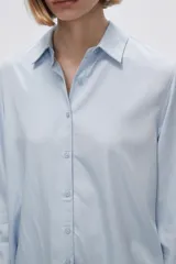 Camisa blanca de manga larga con cuello clásico y cierre frontal con botones. Corte recto y holgado.