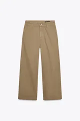 Pantalón cropped color beige de tiro alto y corte recto, confeccionado en algodón. Cuenta con bolsillos delanteros y traseros, trabillas en la cintura y cierre frontal con cremallera y botón.