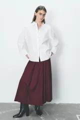 Camisa blanca oversize de popelina de algodón, con cuello solapa, manga larga con puños y cierre frontal con botones ocultos. Detalle de hilo de contraste en los botones.