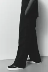 Pantalón cargo negro de corte holgado, con cintura elástica ajustable con cordón, bolsillos laterales al bies, bolsillos tipo cargo con solapa y botón a presión en las piernas y bolsillos traseros con solapa y botón a presión. Cuenta con pliegues cosidos en las rodillas y cordón ajustable oculto en el bajo.