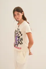Remera color crudo de algodón con estampado de leopardo, hojas de palma y texto 'Rock in the wind'.