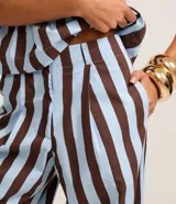 Pantalón de cintura alta, confeccionado en tricolina de algodón, con cierre tradicional, pliegues y rayas verticales en azul claro y marrón.