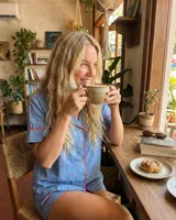 Pijama de dos piezas, compuesto por una camisa de manga corta con cuello solapa y botones frontales, y un short a juego. El conjunto es de color azul claro con un estampado repetitivo de pequeños motivos florales en color rosado/rojo, y ribetes de color rojo en los bordes de la camisa y el short.