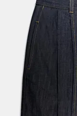 Jeans de tiro alto con corte balloon y largo completo. Presentan cintura con trabillas, bolsillos laterales ocultos, pinzas en el delantero y pespuntes marcados a contraste. Cierre frontal con cremallera, botón y ganchos metálicos.