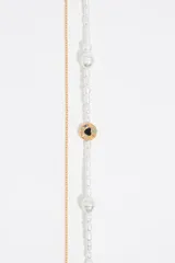 Collar doble con cadena dorada, una con perlas blancas irregulares y otra con una cuenta redonda con un corazón negro en el centro. Cierre con mosquetón y cadena de alargue con dije de corazón. Largo aproximado 52,5 cm.