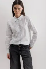 Camisa blanca a rayas verticales negras, de corte clásico, con cuello camisero y mangas largas con puños abotonados.