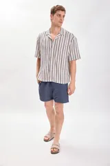 Camisa casual de manga corta con cuello solapa y cierre abotonado. Diseño a rayas verticales en tonos crudo y azul.