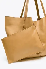 Bolso tipo shopper grande color marrón claro, confeccionado en cuero. Tiene doble asa de hombro y detalle de pespuntes en contraste. Incluye cierre con tiras y botón, y cartera con bolsillo extraíble.