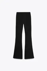 Pantalón negro de tiro alto, confeccionado en tejido elástico con corte ajustado hasta la rodilla y acampanado en el bajo.