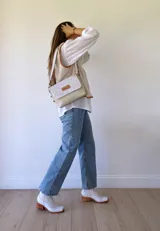 Bandolera color crudo con solapa de gamuza y cuerpo de cuero sintético texturizado. Tiene correa corta de cuero con tientos y forro de tela con bolsillo interno.