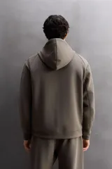 Sudadera con capucha color marrón topo, de corte regular fit, confeccionada en tejido técnico compacto de algodón con elasticidad. Cuenta con cuello subido, manga larga con bolsillo, bolsillos frontales con cierre de cremallera y acabados con rib del mismo tejido.