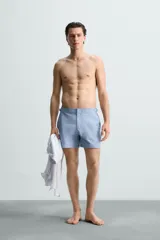 Short de baño celeste de tejido técnico con cintura elástica ajustable con cordón interior y trabillas laterales. Tiene bolsillos frontales y bolsillo trasero con cierre de cremallera. Cuenta con forro interior y cierre frontal con cremallera y botón a presión oculto.