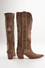 Botas texanas de cuero color marrón con bordados de estrellas y rayos de sol en color blanco. Tiene un pequeño taco de madera y detalles en rojo en el borde superior.