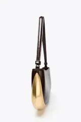 Bolso de hombro marrón oscuro con detalle metálico dorado en un lateral. Tiene un bolsillo interior con cremallera, asa de hombro y cierre con cremallera.