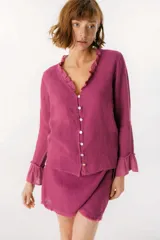 Blusa blanca de lino con botones de nácar, volados en el escote y mangas largas con puños acampanados. Corte recto y holgado.