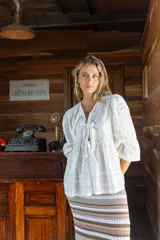 Camisa amarilla con bordado inglés, escote en V, mangas largas abullonadas con puños elásticos y lazos decorativos en el frente.