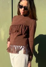 Sweater marrón de punto con cuello redondo y mangas largas. Presenta detalle de flecos en el pecho y en el ruedo.