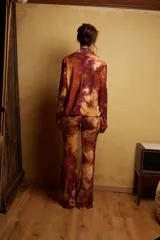 Pantalón de tiro medio con elástico en la cintura y corte acampanado. Diseño con estampado abstracto en tonos marrones, rojizos y amarillos, con textura tipo piel de reptil.