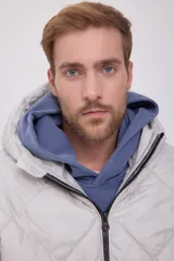 Campera puffer de hombre color gris claro, con capucha ajustable con cordón, cierre de cremallera frontal, bolsillos laterales y mangas largas. Tejido acolchado resistente al viento.